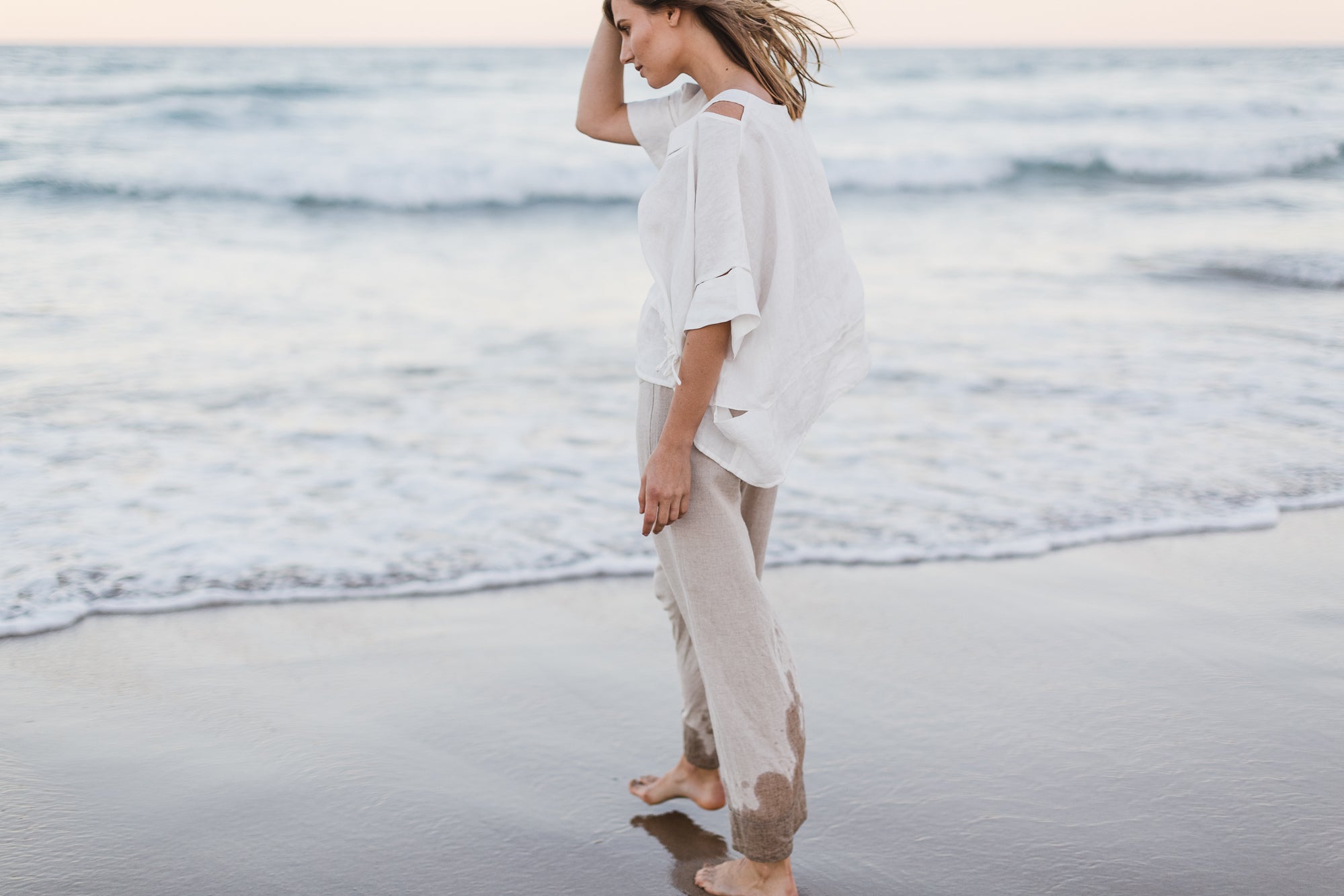 women wearing a baggy white linen shirt on the beach styled with natural coloured linen pants
