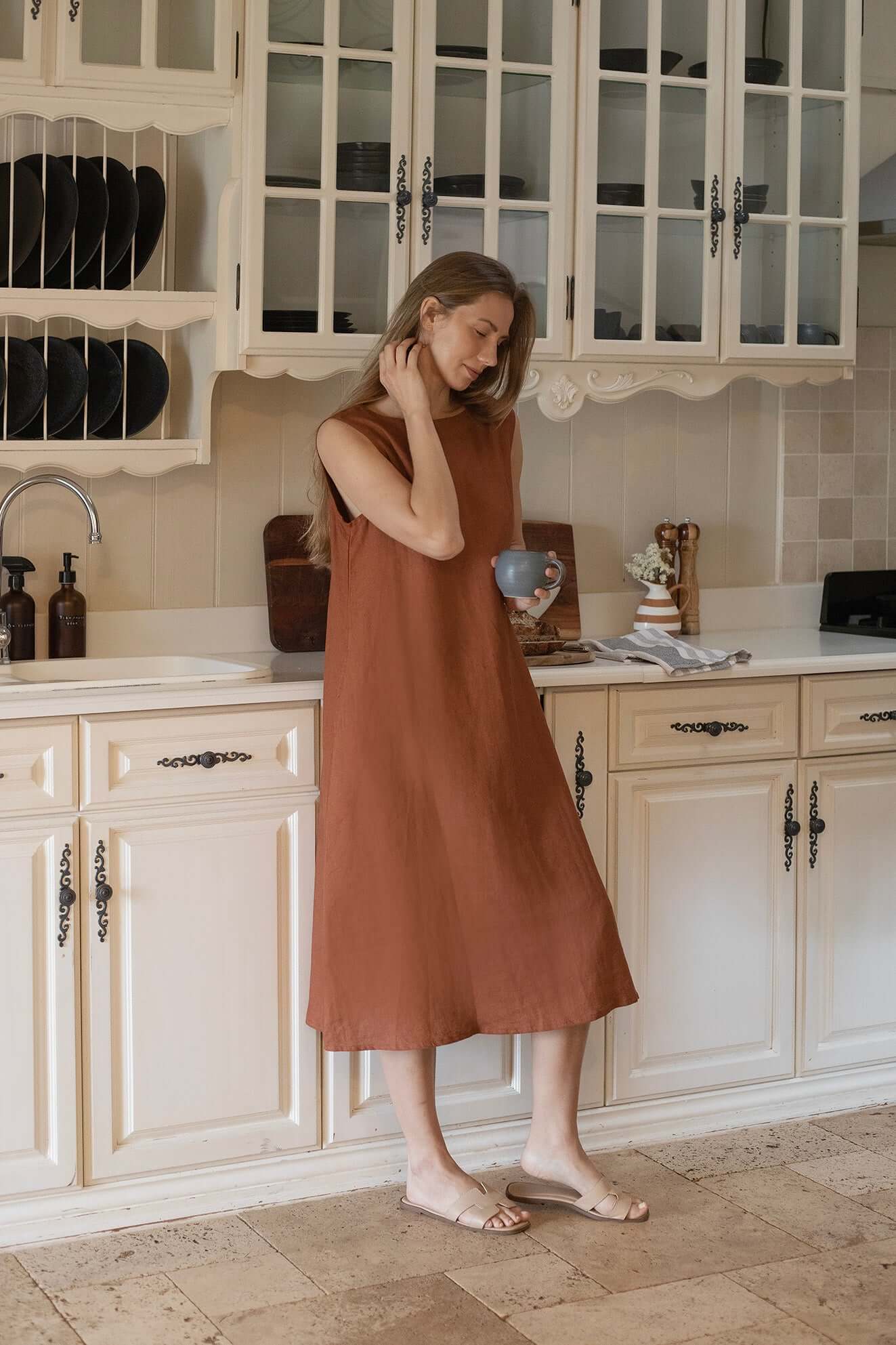Woman in Cynthia Linen Dress Bark enjoying a cup in a stylish kitchen setting.