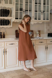 Woman in Cynthia Linen Dress Bark enjoying a cup in a stylish kitchen setting.
