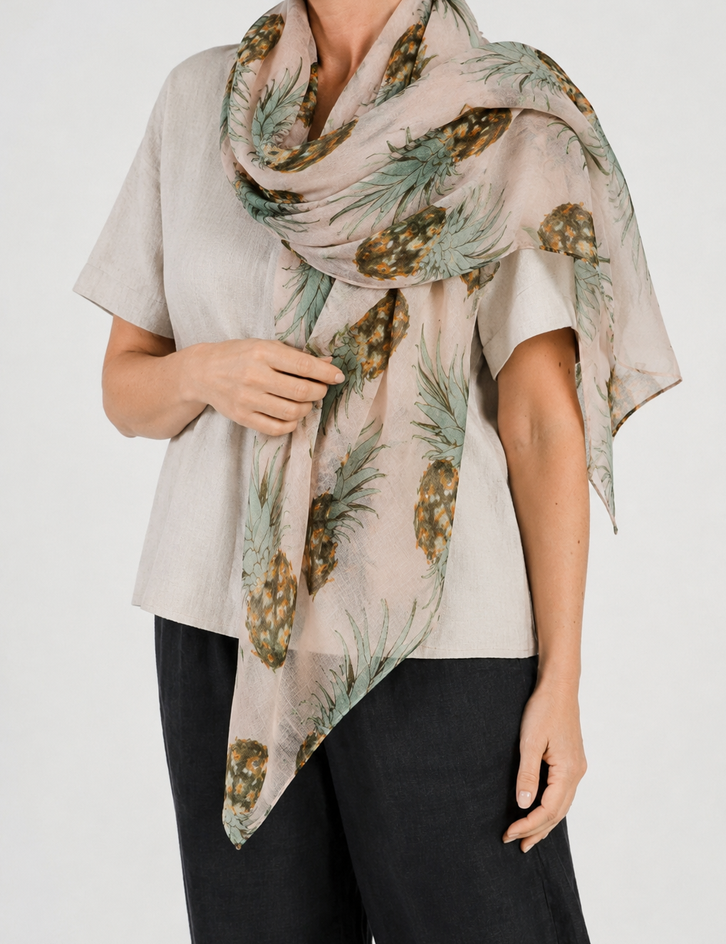 Woman wearing a beige scarf with pineapple pattern on a plain background