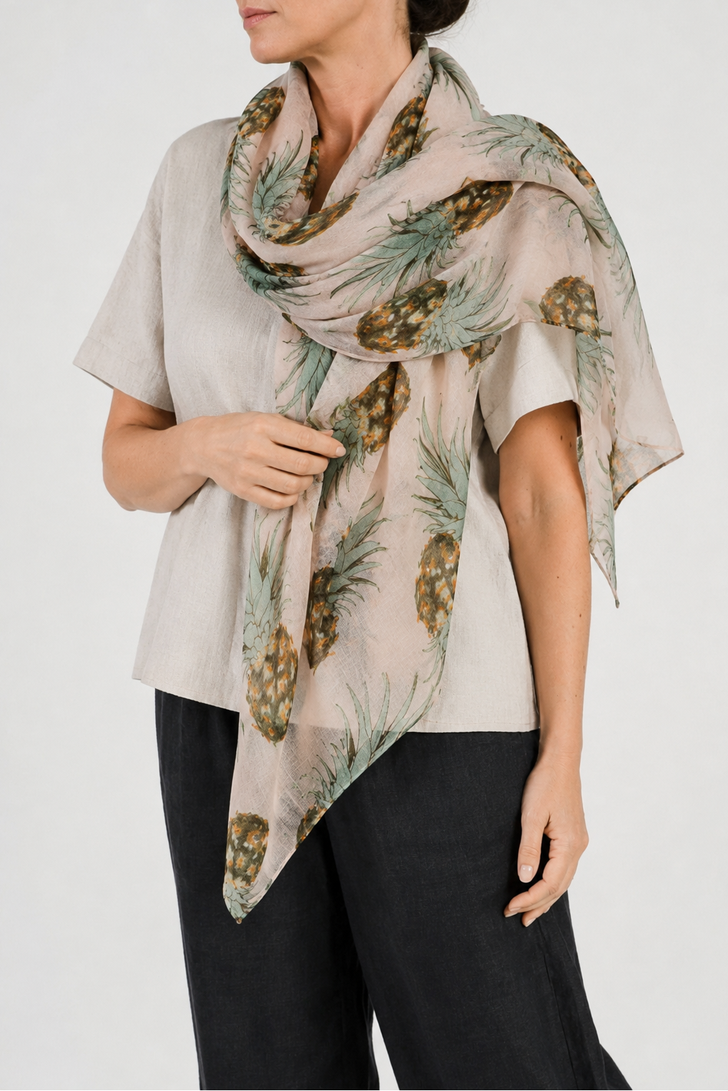 Woman wearing a beige scarf with pineapple pattern on a plain background