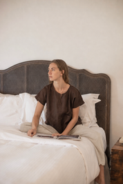 Model wearing Zoe Linen Top Cocoa whilst sitting on bed.